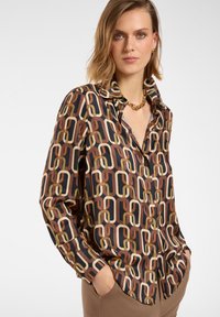 Button-up shirt with a geometric chain pattern in brown, beige, and orange on a black background; made of smooth fabric with a collar.