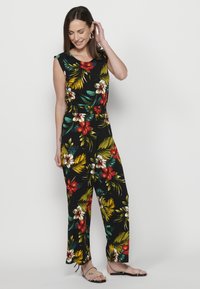 Jumpsuit floreale nero con fiori rossi, gialli e bianchi. Presenta maniche corte, vita aderente e design a gamba larga.