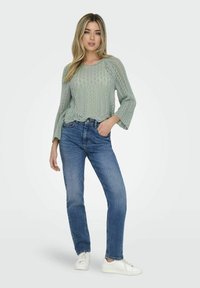 Pullover lavorato a maglia di un verde chiaro, con un motivo testurizzato, vestibilità comoda e maniche a tre quarti, abbinato a jeans blu a gamba dritta e sneakers bianche.
