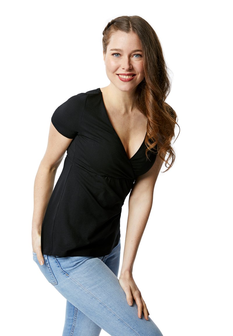 Schwarzes, kurzärmliges Oberteil mit V-Ausschnitt und geraffter Taille, getragen mit hellblauen Jeans. Das Model hat welliges braunes Haar und einen neutralen Hintergrund.