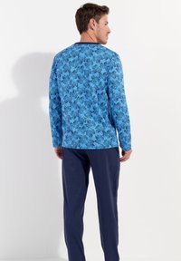 Langarmshirt in Blau mit floralem Muster, kombiniert mit marineblauen Hosen. Hat einen runden Ausschnitt und eine lässige Passform. Hergestellt aus weichem Stoff.