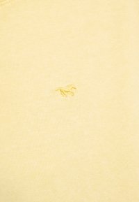 Žltá látka s malým vyšívaným motívom bežiaceho koňa uprostred povrchu.