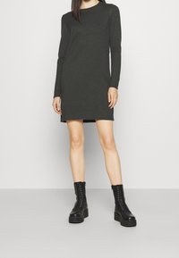 Dark green knitted dress with long sleeves and ribbed edges, paired with black lace-up boots. The fabric appears thick and textured.