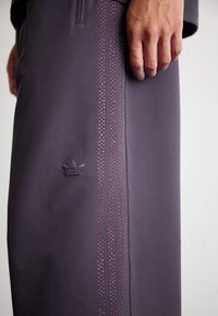 Vijolične športne hlače z tremi navpičnimi črtami okrašenimi z majhnimi roza rhinestones in toniranim vezenim logotipom na nogi.