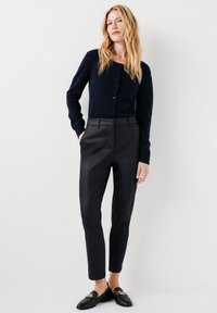 Marinblå cardigan med knappstängning, i kombination med skräddarsydda svarta byxor och mockasiner med kedjeaccent. Slät textur, figursydd design.