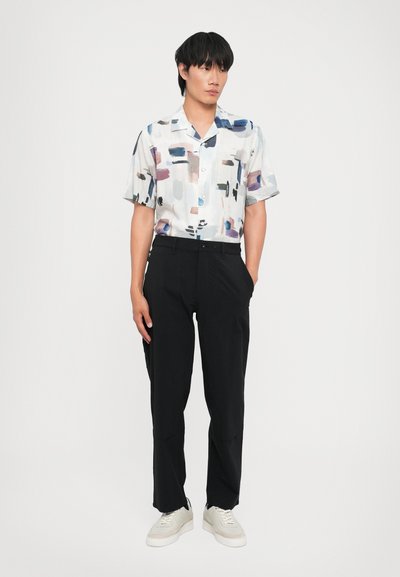 Camisa de manga corta con un patrón abstracto en tonos pasteles de azul, rosa y negro, combinada con pantalones negros y zapatillas blancas.