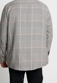Camisa de cuadros en blanco y negro con detalles en naranja. Mangas largas, cuello clásico y cierre delantero de botones. Tejido suave con un ajuste estructurado.