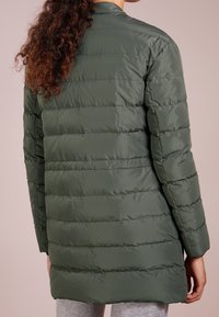 Polstrovaná, dlouhá olivově zelená bunda s hladkou, lesklou texturou a horizontálním prošíváním. Má dlouhé rukávy a minimalistický design.