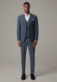Grijze geruite pak met notch revers, drie-knopen vest en slim-fit broek. Witte overhemden en zwarte schoenen maken de look compleet.