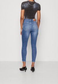 Top negro de manga corta combinado con jeans skinny de tiro alto en azul; los vaqueros presentan una textura desgastada y un sutil detalle en los bolsillos traseros.