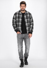Czarna i biała kurtka w kratę z czarną koszulą, szarymi dżinsami i czarnymi sznurowanymi butami. Kurtka ma luźny kołnierz i zapięcie na guziki.