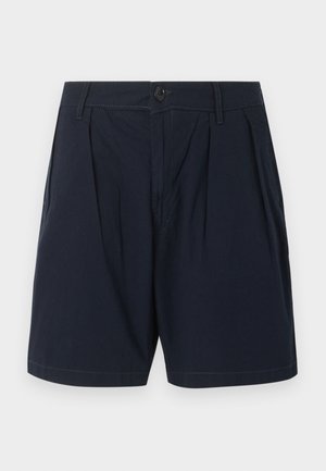Mørk navy høytlivsshorts med frontfolder, knappelukking, beltehemper og sidelommer mot en ensfarget lys bakgrunn.