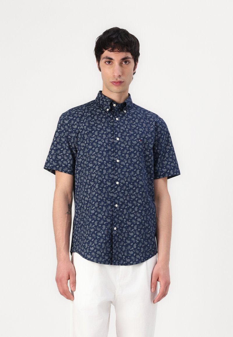 Chemise à manches courtes, boutonnée, en bleu marine avec un motif paisley. Fabriquée en tissu léger, elle dispose d'un col standard et d'une poche poitrine.