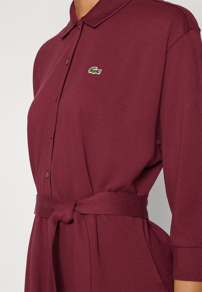 Burgunderfarbendes Polo-Kleid aus strukturiertem Stoff, mit einem Kragen, Knopfverschluss und einem gebundenen Taillengürtel, versehen mit einem kleinen gestickten Logo.
