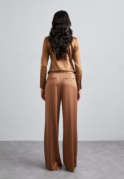 Blouse en satin marron et pantalons larges, tous deux présentant une texture lisse. Les pantalons ont des poches arrière, et la blouse a des détails de boutons sur les manches.