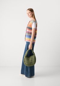 Mehrfarbiger Strickwesten mit Knopfverschluss, kombiniert mit blauen weiten Jeans und einer grünen gesteppten Handtasche. Glatte Textur und lockere Passform.