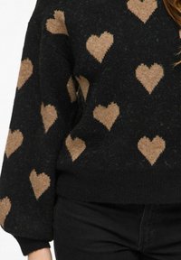 Czarny sweter z teksturowanym wykończeniem, ozdobiony powtarzającym się wzorem średniej wielkości beżowych serc. Ściągacze przy mankietach i na dole swetra.