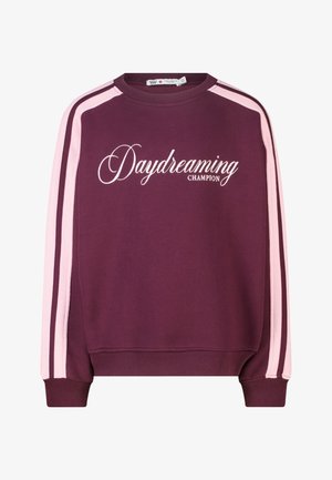 Sweat-shirt bordeaux avec des rayures rose clair sur les manches et un texte blanc en cursive "Daydreaming Champion" sur le devant.