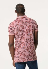 Polo shirt met korte mouwen in lichtroze met een bladerenpatroon in rood en bruin, met een effen kraag en contrasterende afwerking op de mouwen.