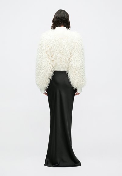 Λευκό χνουδωτό κοντό μπουφάν με μακριά μανίκια πάνω από εφαρμοστή μαύρη σατέν φούστα, που αναδεικνύει υφή και ρέουσα σιλουέτα.