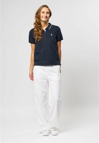 Marineblå polo med hvide detaljer, med klassisk krave og korte ærmer. Sammen med løstsiddende hvide bukser og hvide sneakers.