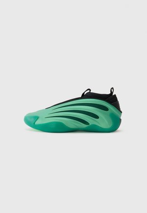 Sneaker mit einem eleganten Design, ausgestattet mit einer grünen Gummisohle und einem schwarzen Textil-Obermaterial. Geschwungene Linien erzeugen einen dynamischen Look.