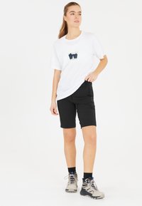Vit t-shirt med bergsgrafik, svarta shorts med sidofickor och beiga vandringsskor med grå sulor. Enkel och funktionell design.