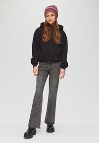 Zwarte hoodie met een ontspannen pasvorm, grijze flared jeans en zwarte platformlaarzen. Het model draagt een kastanjebruine gebreide beanie.