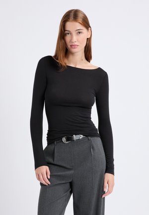 Top negro de manga larga con escote barco, que presenta un diseño ajustado. Combinado con pantalones grises de talle alto y un cinturón negro con detalles plateados.
