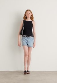Svart ermeløs topp, lyseblå denimshorts med mønstrete tekstur, svart veske og svarte sandaler. Nøytral bakgrunn.