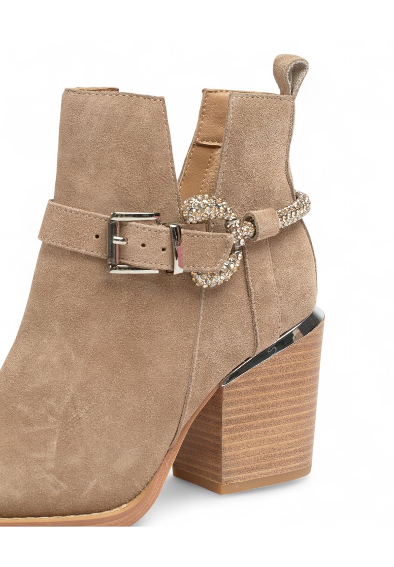 Beige suède enkelboot met een ronde neus, een decoratieve zilveren gesp met rhinestones en een gestapeld houten hak.