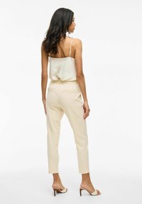 Beige stretchbroeken met elastische taille, zijzakken en taps toelopende pijpen, gecombineerd met een licht zijden cami-top en naakte block-heeled sandalen.