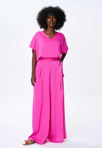 Fuksjowy dwuczęściowy zestaw składający się z luźnej bluzki z dekoltem w kształcie litery V oraz spodni z wysokim stanem i szerokimi nogawkami z bocznymi kieszeniami.