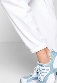 Vita, joggers med elastiska muddar och texturerad yta, tillsammans med ljusblå träningsskor som har nätpaneler och vita detaljer.