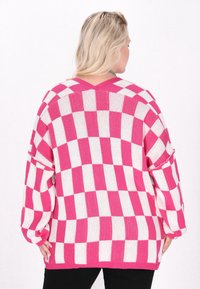 Rosa och vit rutad stickad tröja med långa ärmar, v-ringad och ribbad nederkant. Har en lös passform och texturerat mönster.