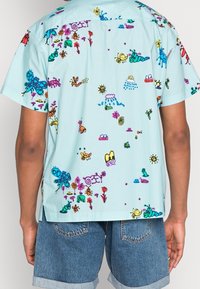 Camicia a maniche corte di colore azzurro chiaro con un motivo colorato e giocoso di insetti e fiori. Realizzata in tessuto leggero con una vestibilità morbida.