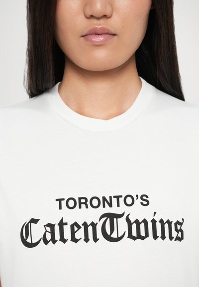 Bijela pamučna majica s kratkim rukavima na kojoj se nalazi crni natpis "TORONTO'S CatenTwins" u podebljanom, dekorativnom fontu.