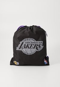 Sac à dos en nylon noir avec des accents violets. Présente un logo à rayures blanches pour les Los Angeles Lakers et une étiquette de la NBA.
