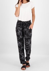 Schwarze Hosen mit weißen Blattmustern, ausgestattet mit einem elastischen Bund, Kordelzug und Seitentaschen. Kombiniert mit einem weißen Kurzarmoberteil.
