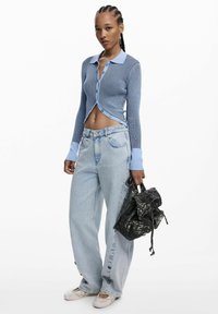 Cardigan albastru deschis cu mâneci lungi �și dungi, cu guler tip rever, asortat cu blugi largi albastru deschis și rucsac negru cu model.