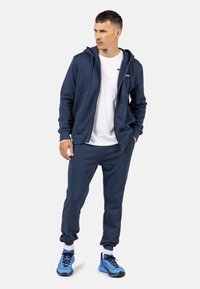 Navyblaue Zip-Hoodie und passende Jogging-Hosen aus weichem Stoff, kombiniert mit hellblauen Sportschuhen. Einfaches Design, elastische Bündchen und Gummizug.