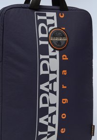 Marinen nylon rygsæk med kontrastfarvet hvid og orange grafisk print samt rundt logo-patch, der har sorte bærehåndtag og tekstureret overflade.