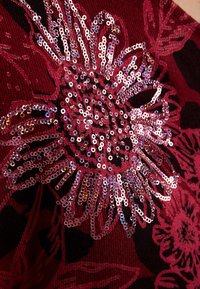 Tissu rouge avec un grand motif floral orné de paillettes roses brillantes, créant un motif texturé et réfléchissant.