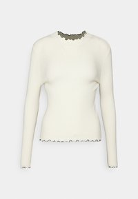 Långärmad figurnära vit ribbad tröja med svart kantad volangkrage, ärmslut och nederkant mot en enfärgad bakgrund.