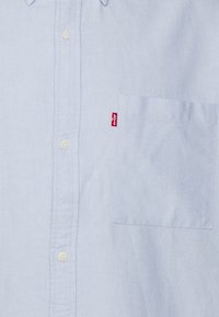 Vaaleansininen nappipaita, jossa on rintatasku oikealla puolella ja pieni punainen Levi's-tagi.