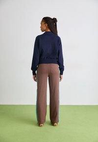 Marineblauer Pullover mit gerippten Bündchen und Saum, kombiniert mit braunen Hosen mit türkisfarbenen Seitenstreifen. Glattes Material, lockere Passform. Rückansicht.