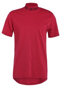 Camiseta roja de manga corta con cuello alto que presenta texto en negro. Está hecha de un tejido suave, tiene un dobladillo curvado y un corte relajado.