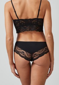 Schwarzes Spitzen-Bralette und passender Slip. Das Bralette hat einen gewellten Saum und verstellbare Träger; der Slip hat eine Spitzenkante und ein nahtloses Design.