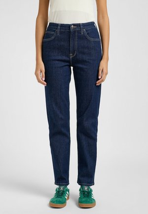 Jeans in denim blu scuro con design a gamba dritta, dotati di cinque tasche, cuciture chiare e vita alta, abbinati a sneaker verdi.