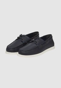 Scarpe da barca in pelle blu navy con suole in gomma bianca e dettagli con lacci su uno sfondo grigio chiaro uniforme.